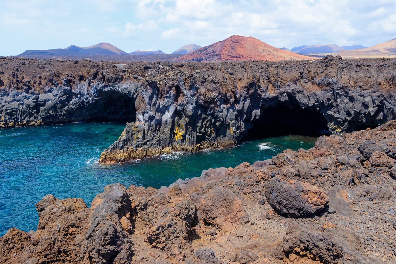 Los Hervideros: la costa di lava dove il mare entra nelle grotte, con i vulcani di Timanfaya sullo sfondo