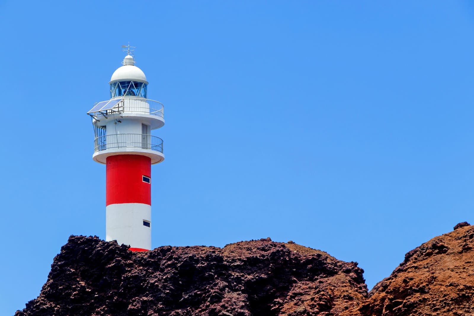 Il faro bianco e rosso di Punta de Teno sulla roccia vulcanica, contro il cielo blu