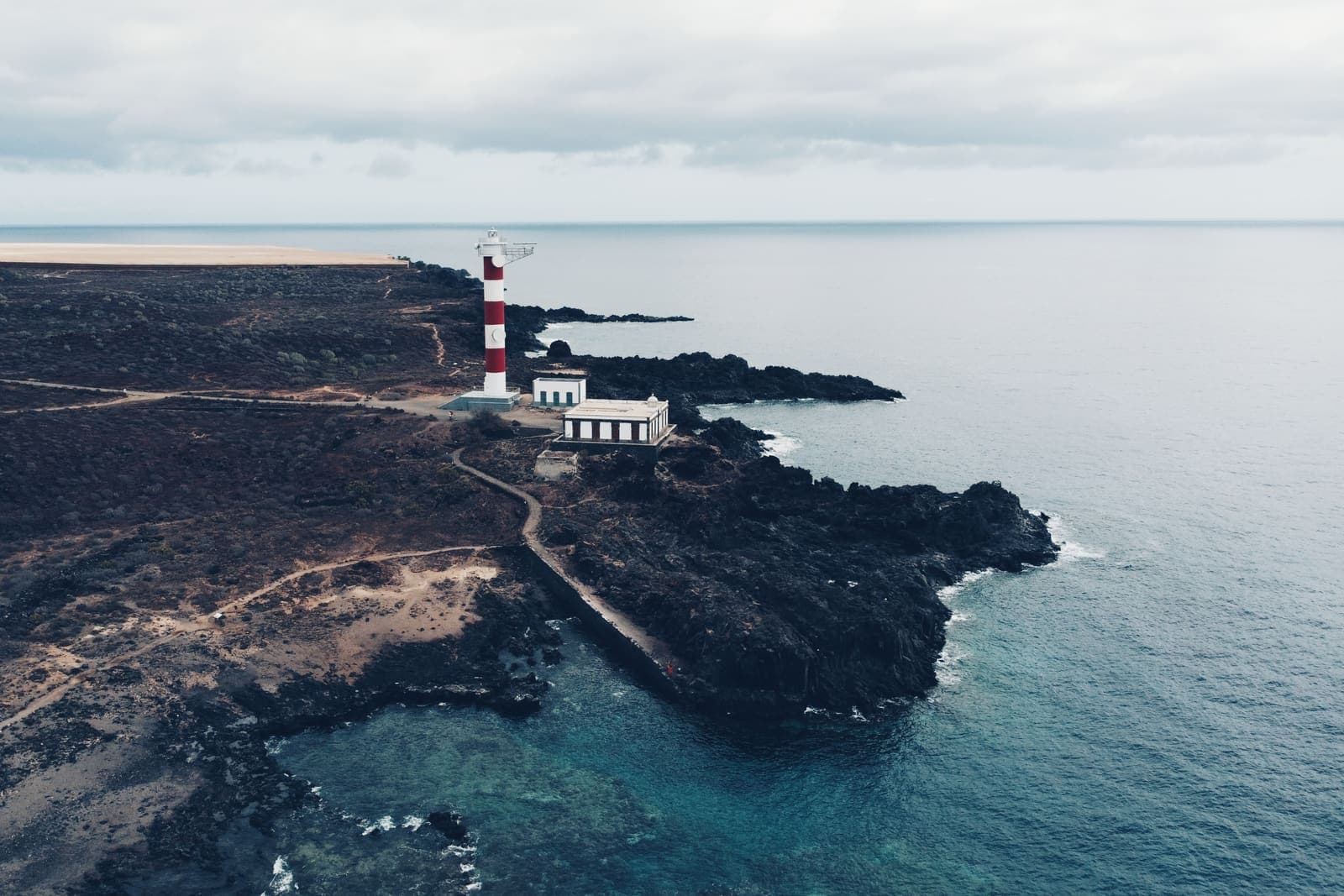 Il faro bianco e rosso di Rasca sulla costa di lava nera del Malpaís, visto dall'alto