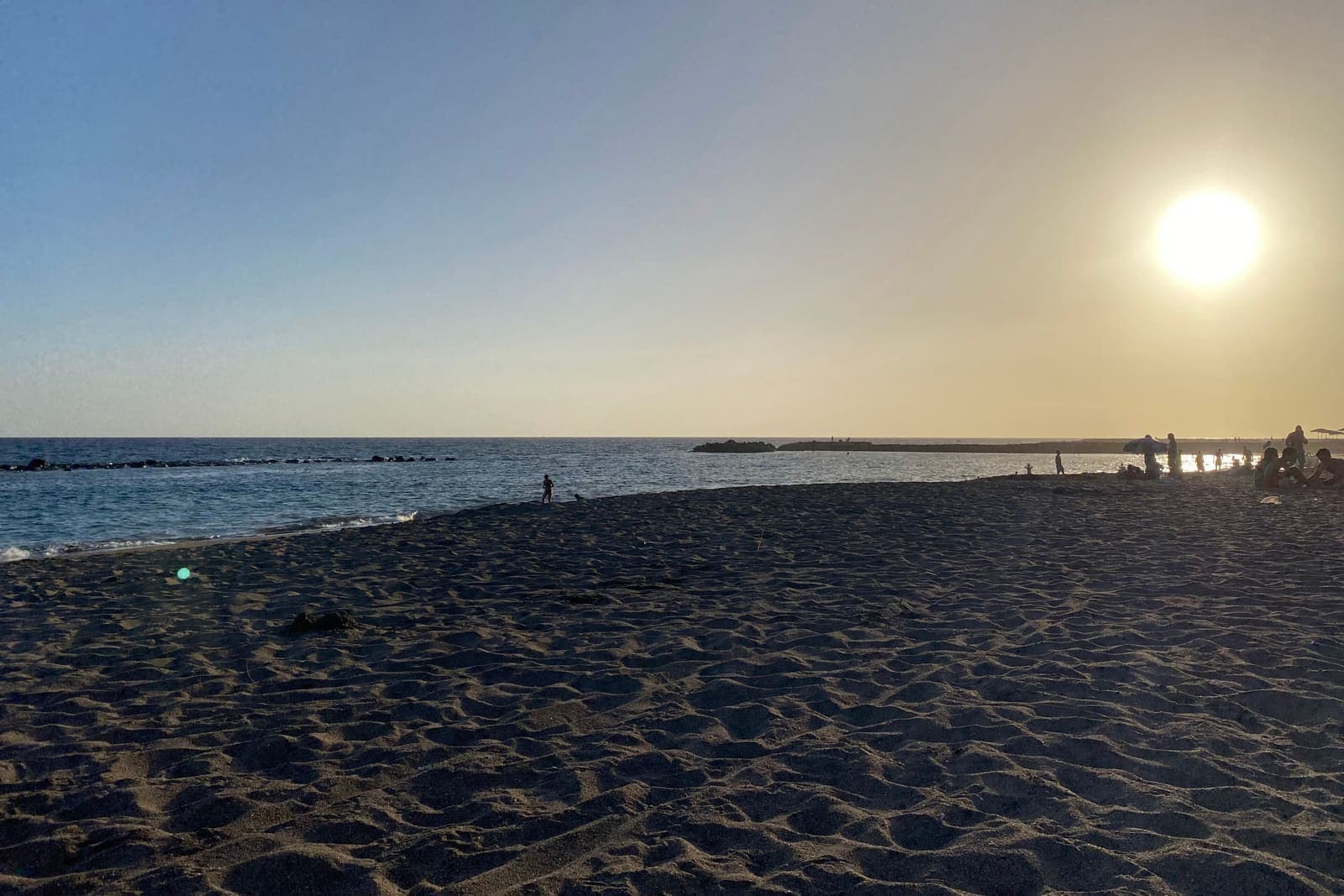 Playa del Duque a Costa Adeje al tramonto, con il sole basso sul mare e la sabbia in primo piano